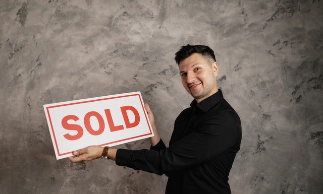 man holding "sold" sign